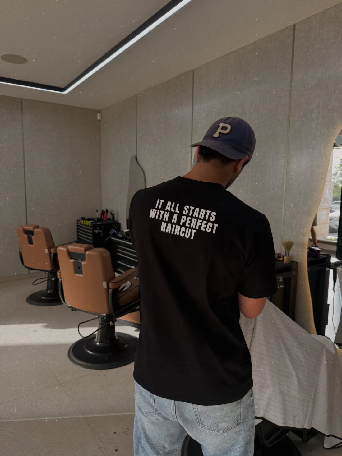 ספר בחולצת 'It all starts with a perfect haircut' עובד במספרת YN, כיסאות עור קוניאק ברקע